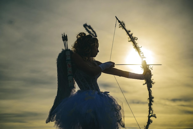 Silueta de un cupido. Vista lateral de la arquera adolescente contra la puesta de sol. Feliz día de San Valentín.