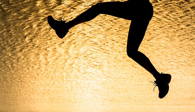 Foto silueta, de, homem jovem, pular, praia, em, pôr do sol