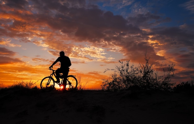 Silueta de deportista en bicicleta por el prado en la hermosa puesta de sol.