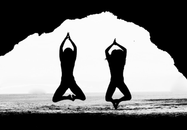 Foto silueta de dos mujeres jóvenes con las manos juntas saltando en la playa