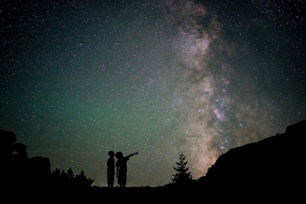 Foto silueta de dos niños pequeños con la vía láctea y hermoso cielo nocturno lleno de estrellas en el fondo