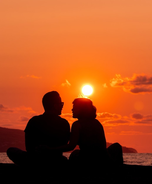 Foto silueta de dos personas en el amor al atardecer y sentadas divirtiéndose