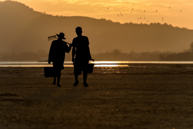 Silueta Dos personas caminando en la playa al atardecer.