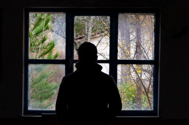 Una silueta dramática de un hombre capturada desde atrás en una foto retroiluminada frente a una ventana rota