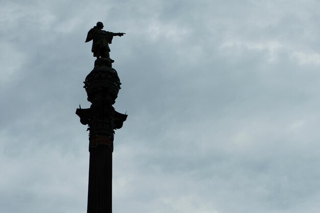 Silueta de la estatua de Cristóbal Colón con la mano apuntando en dirección a América desde Barcelona España Moody cielo gris en el fondo