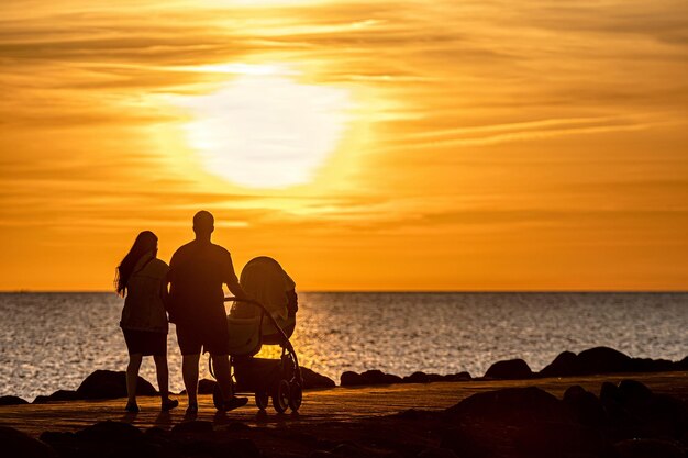 Foto silueta de una familia caminando por el muelle durante la hora dorada de la puesta de sol