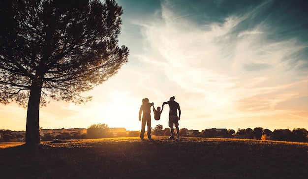 Silueta de familia feliz caminando en el prado al atardecer - Madre, padre e hijo niño divirtiéndose al aire libre disfrutando de tiempo juntos - Familia, amor, salud mental y concepto de estilo de vida feliz