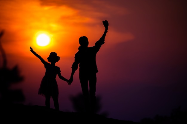 Silueta de una familia con una madre feliz jugando con una niña en el cielo del atardecer