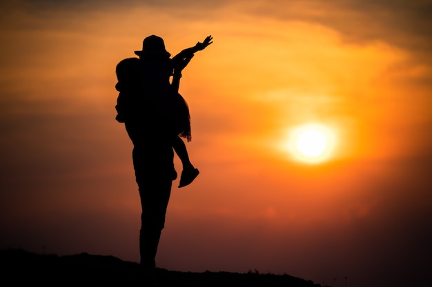 Silueta de una familia con una madre feliz jugando con una niña en el cielo del atardecer