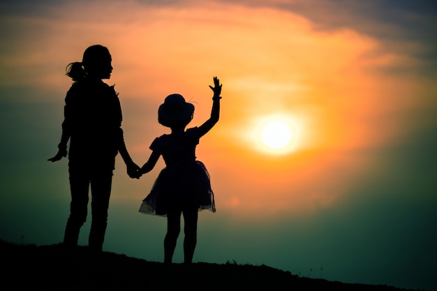 Silueta de una familia con una madre feliz jugando con una niña en el cielo del atardecer