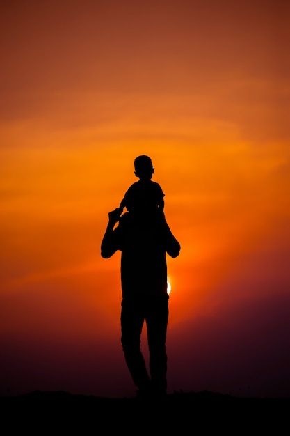 Silueta de una familia con un niño montando felizmente el cuello de su padre contra el cielo del atardecer