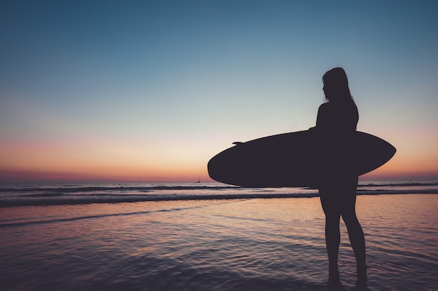 silueta femenina con tabla de surf en la playa al atardecer