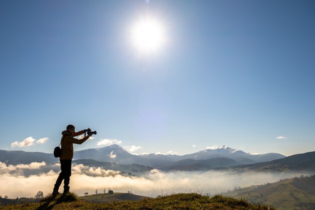 Silueta de un fotógrafo mochilero tomando fotografías del paisaje matutino en las montañas de otoño