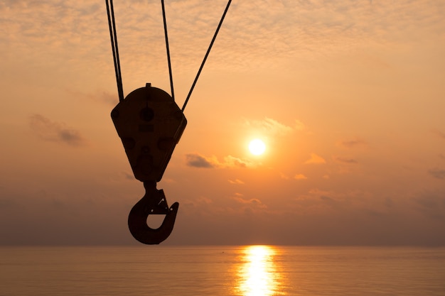 silueta de gancho de la grúa en la hora del atardecer con el fondo del mar en la plataforma de petróleo y gas en alta mar