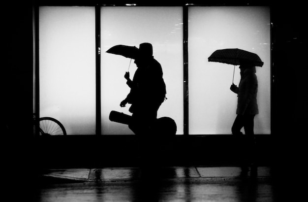 silueta de gente caminando bajo la lluvia con paraguas y una guitarra en la ciudad