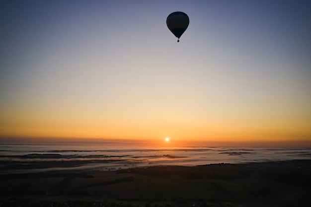 Silueta de un globo de aire caliente sobre un fondo de cielo azul al amanecer con niebla