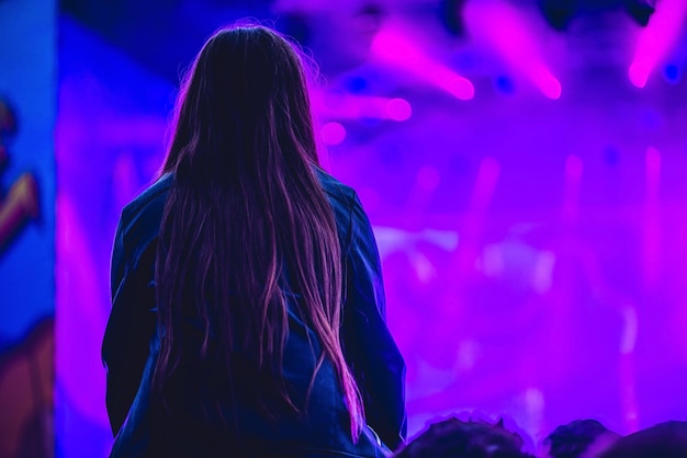 Silueta de una gran multitud en concierto contra un escenario brillantemente iluminado. Concierto de rock nocturno con gente divirtiéndose levantando las manos en el aire y animando a los músicos.