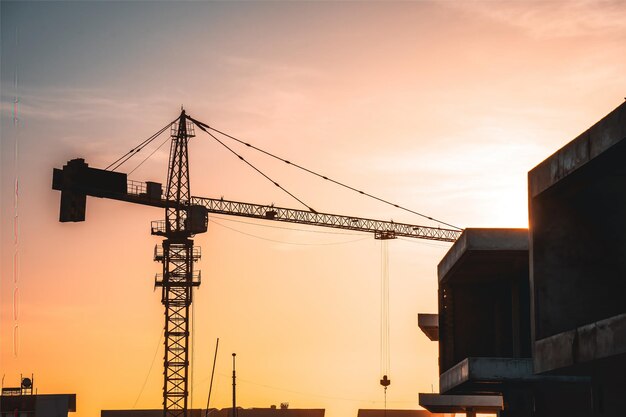 Silueta Grúa de construcción en el fondo del cielo puesta de sol Sitio de construcción Gran sitio de construcción que incluye varias grúas que trabajan en un complejo de edificios con un cielo amarillo claro y el sol