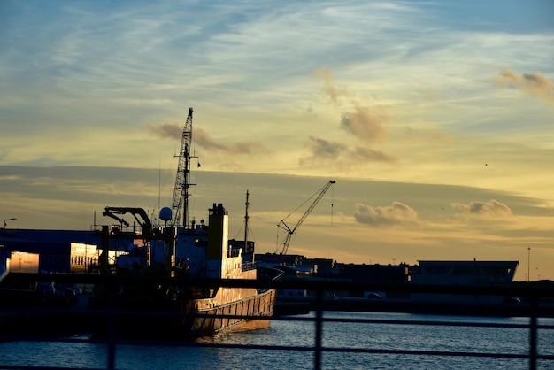 Silueta de grullas en el puerto contra el cielo nublado durante la puesta de sol