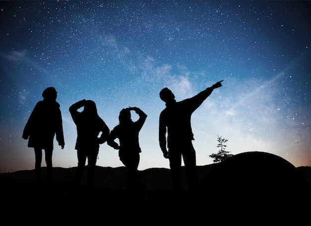 Una silueta de grupo de personas se divierten en la cima de la montaña cerca de la carpa