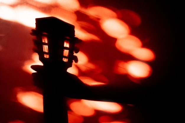 Foto silueta de una guitarra acústica sostenida por las manos sobre un fondo de pared rojo con luz solar reflejada