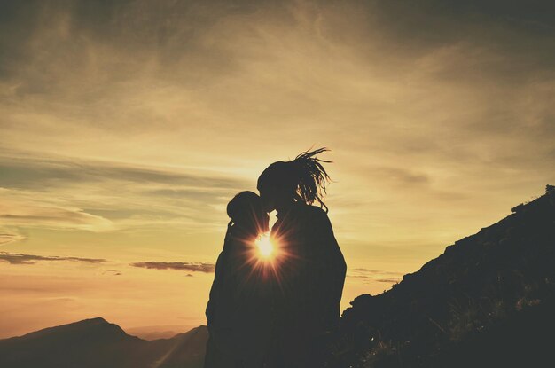 Foto silueta de un hombre besando a una mujer contra el cielo durante la puesta de sol