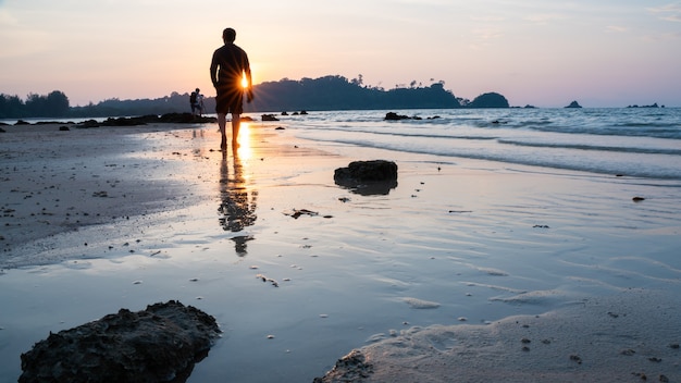 Silueta de hombre caminando por la playa al atardecer