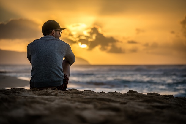 Silueta de hombre caucásico sentado en Sunset Beach en Hawaii mirando la puesta de sol sobre el océano