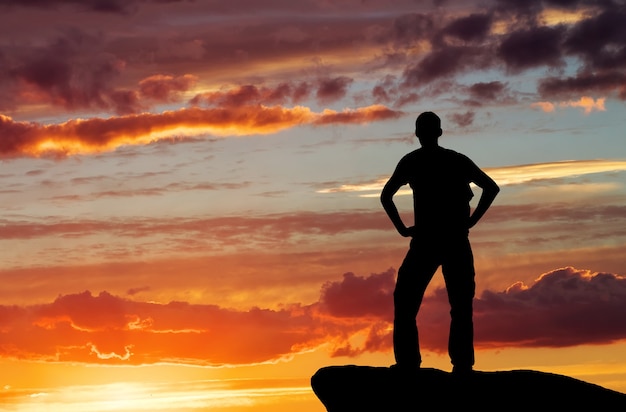 Foto silueta de un hombre en la cima de una montaña en el fondo del cielo al atardecer