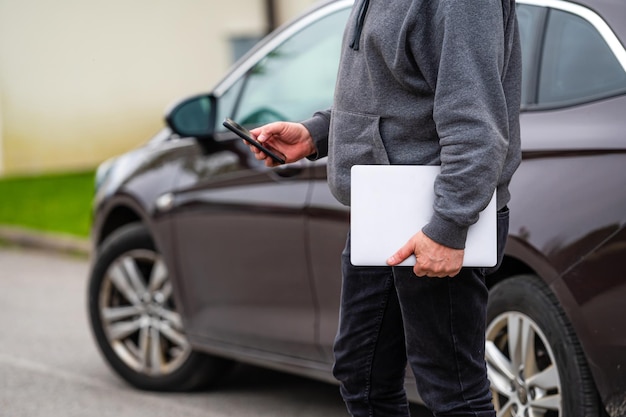 Una silueta de un hombre con una computadora y un teléfono en sus manos en el fondo de un vehículo estacionado