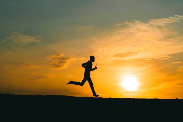 Silueta de un hombre corriendo en un camino rural durante la puesta de sol
