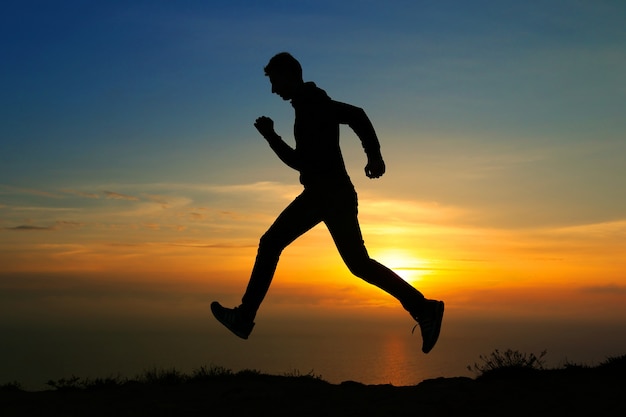 Silueta de hombre corriendo contra el cielo colorido. Silueta de hombre corriendo sobre fondo ardiente al atardecer