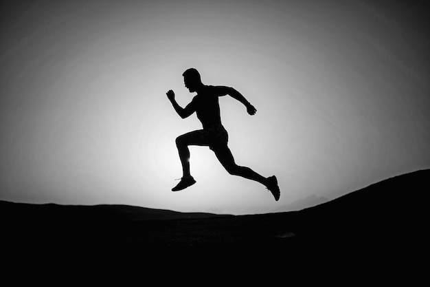 Silueta de hombre corriendo en el fondo del cielo ardiente del atardecer en el futuro del deporte y la recreación de montaña y la gente de éxito y la velocidad de la naturaleza y el estilo de vida saludable