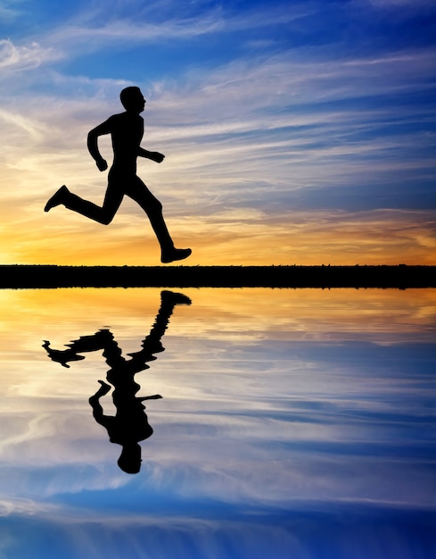 Foto silueta de hombre corriente contra el cielo colorido. silueta de hombre corriendo al atardecer. reflexión del agua. elemento de diseño.