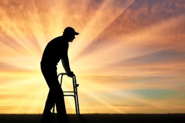 Silueta de un hombre discapacitado caminando, usando un andador para discapacitados. El concepto de ancianos y discapacitados