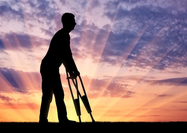 Silueta de un hombre discapacitado con muletas caminando contra la puesta de sol. El concepto de personas con discapacidad con muletas.