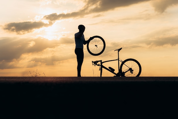 Silueta de hombre fuerte en casco y rueda de fijación de ropa deportiva en bicicleta al aire libre