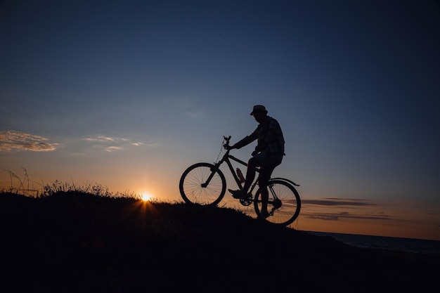 Silueta de un hombre hipster en una bicicleta en el fondo del atardecer