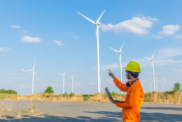 Silueta de hombre ingeniero trabajando y sosteniendo el informe en la estación generadora de energía de la granja de turbinas eólicas en la gente de mountainThailand