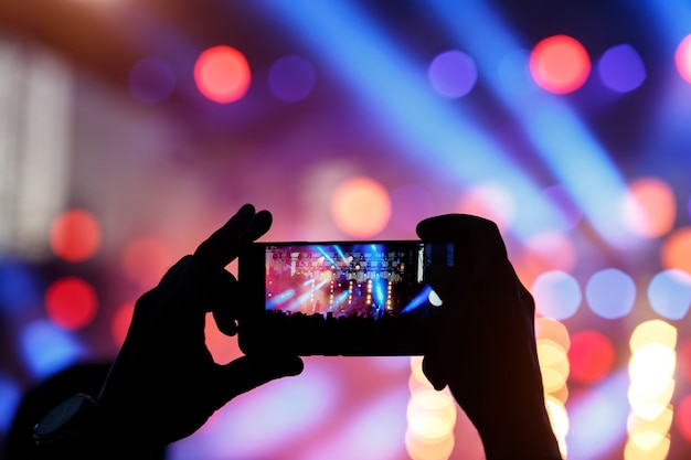 Silueta de hombre joven, tomando foto concierto de rock en el teléfono móvil, fiesta al aire libre