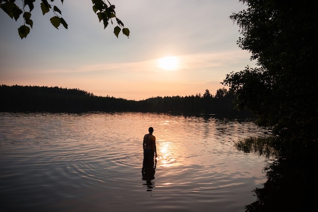 Silueta de hombre en el lago en reflejo de la puesta de sol, cuerpo de agua entre los árboles.