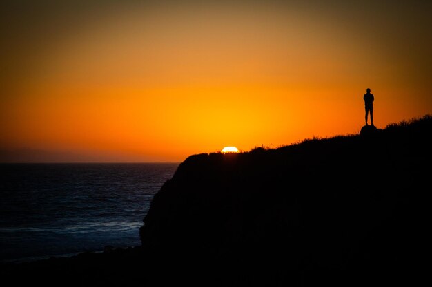 Foto silueta de un hombre mirando al mar contra el cielo durante la puesta de sol