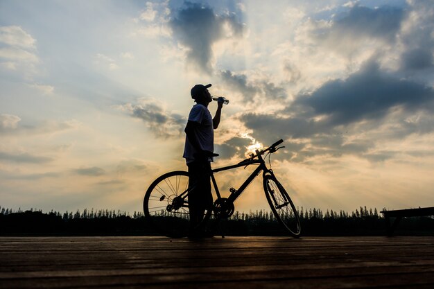 silueta del hombre en el momento de la puesta del sol del lago después del intenso entrenamiento en bicicleta