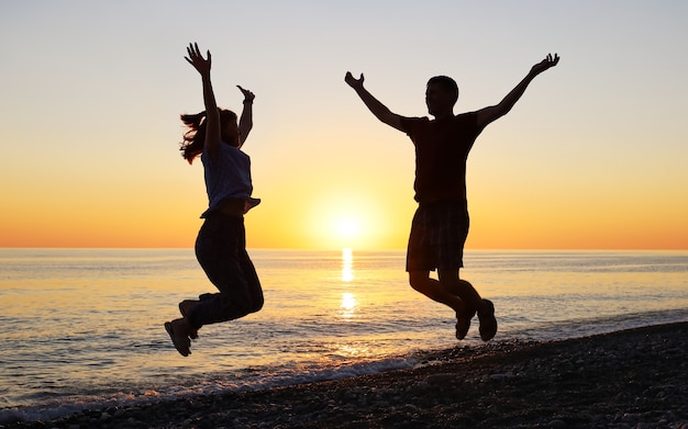 Silueta de hombre y mujer saltando de alegría al atardecer en la playa desierta del mar
