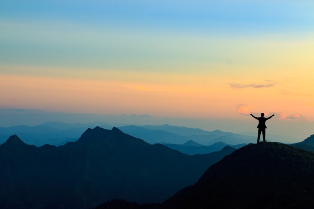 Silueta de hombre de negocios en la cima de la montaña sobre fondo de cielo al atardecer, concepto de negocio, éxito, liderazgo y logro