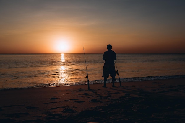 Silueta de un hombre pescando sobre un fondo de hermosa puesta de sol colorida junto al agradable mar en la playa de arena.