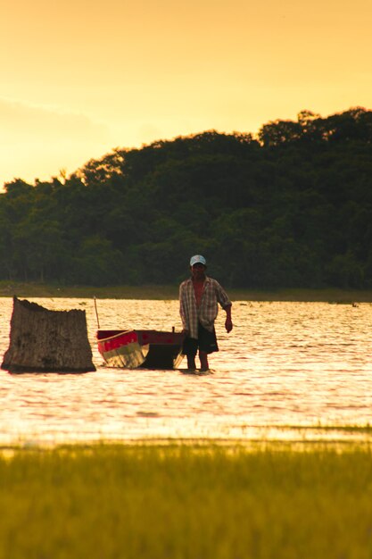 Foto silueta de un hombre de pie en el agua junto a su barco