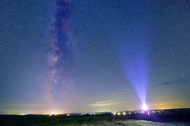 Silueta de un hombre y un rastro de una linterna sobre un fondo de cielo estrellado con h parte de la galaxia Vía Láctea.