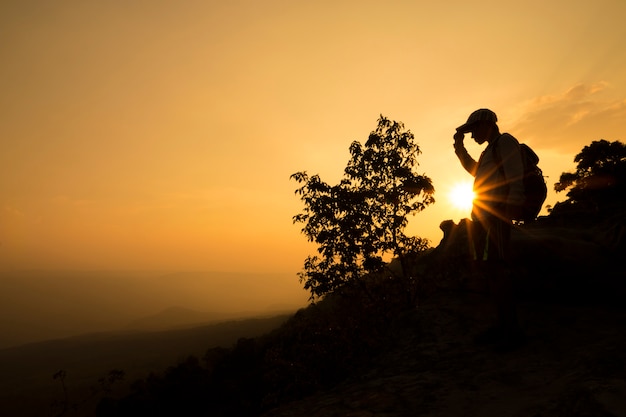 silueta de un hombre relajarse en el acantilado y las montañas con puesta de sol en la noche