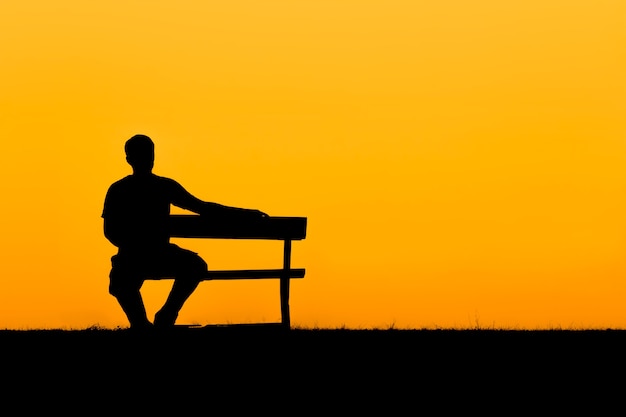 Foto una silueta de hombre sentado en un banco en puesta de sol